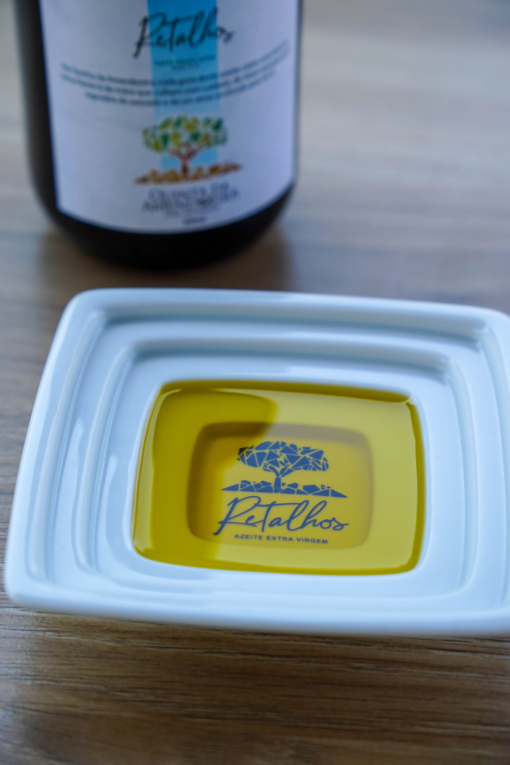 Close-up of a white container with a bright yellow inner tray on a wooden surface, a blurred olive oil bottle in the background.